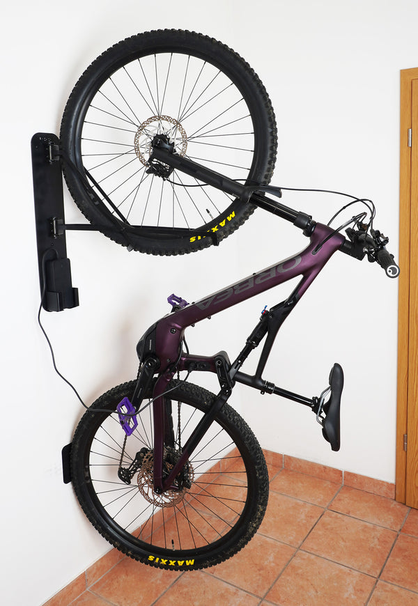 Purple bicycle mounted on a wall-mounted bike rack against a white wall.