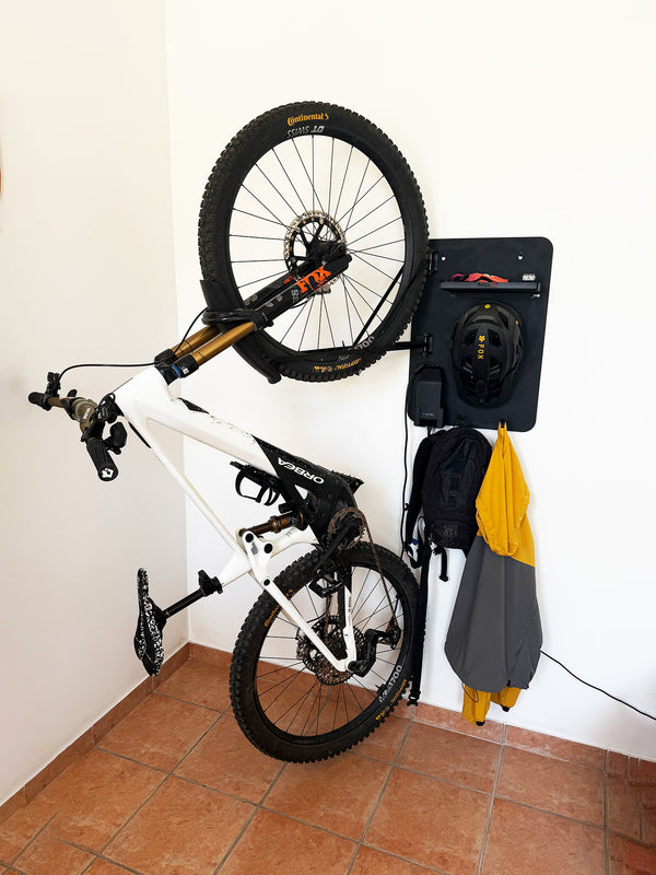 Folded bicycle against a white wall with a helmet and raincoat hanging on hooks.
