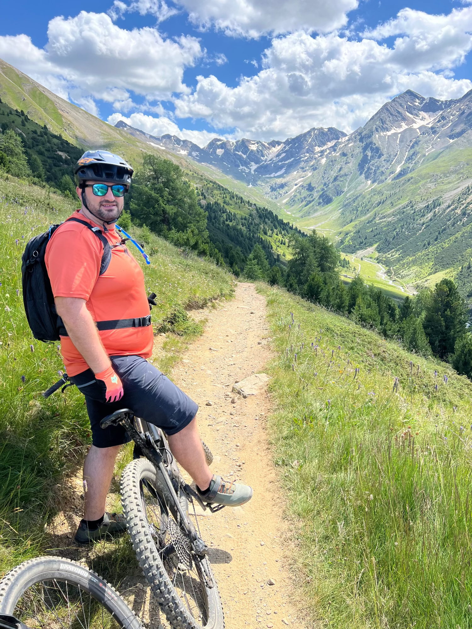 Man with a bicycle on a mountain path with scenic mountains in the background